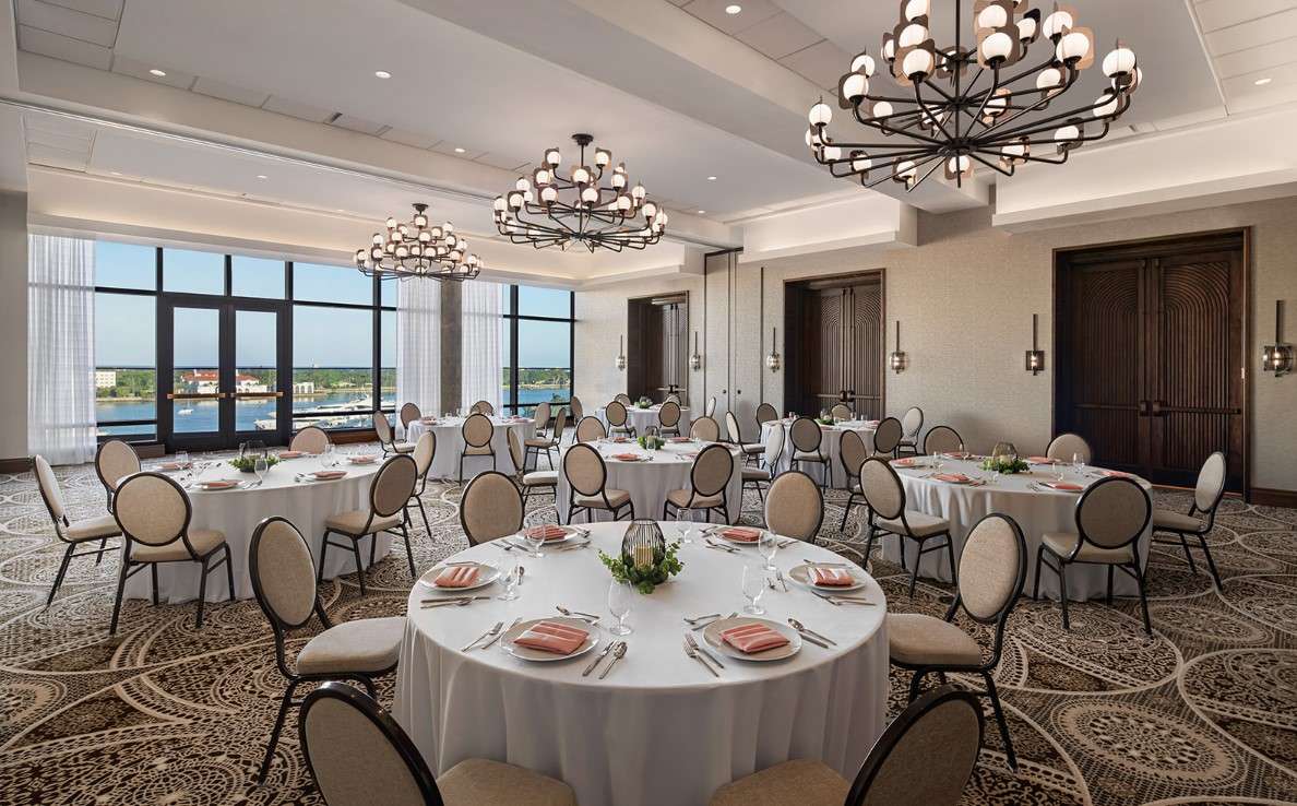 The Blue Heron Ballroom at The Ben, set with round tables, white linens, and chandeliers, overlooking the Intracoastal marina.