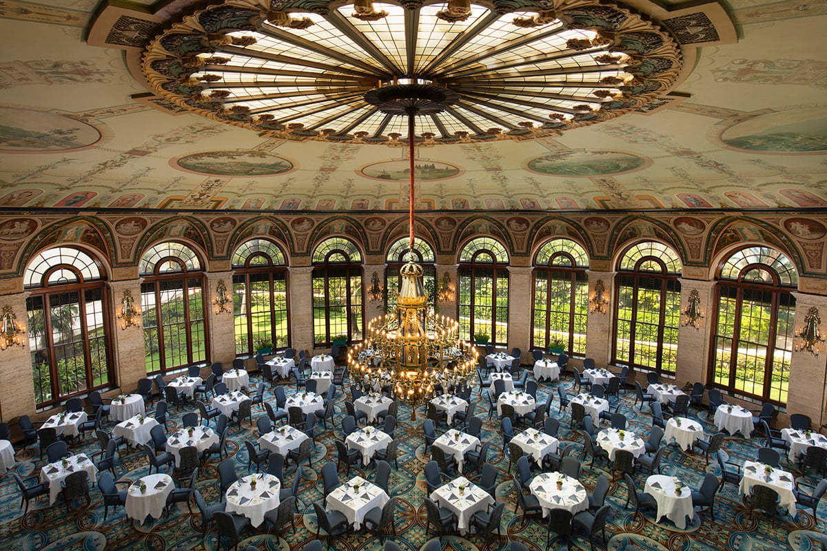 The Circle Ballroom at The Breakers, a round room with a domed stained-glass ceiling, frescoed walls, and tables set for dinner beneath a grand chandelier.