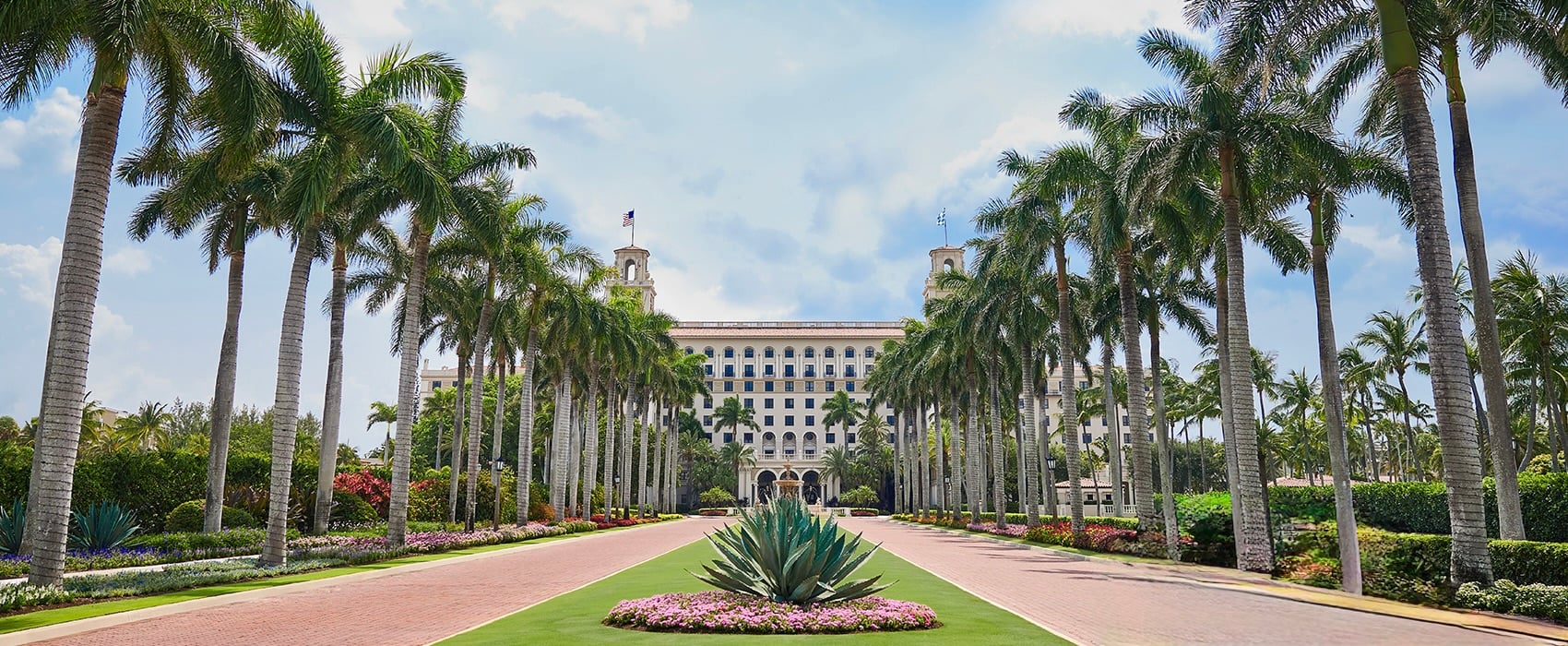 The palm-lined entrance drive leading to The Breakers' Italian Renaissance facade and twin belvedere towers.