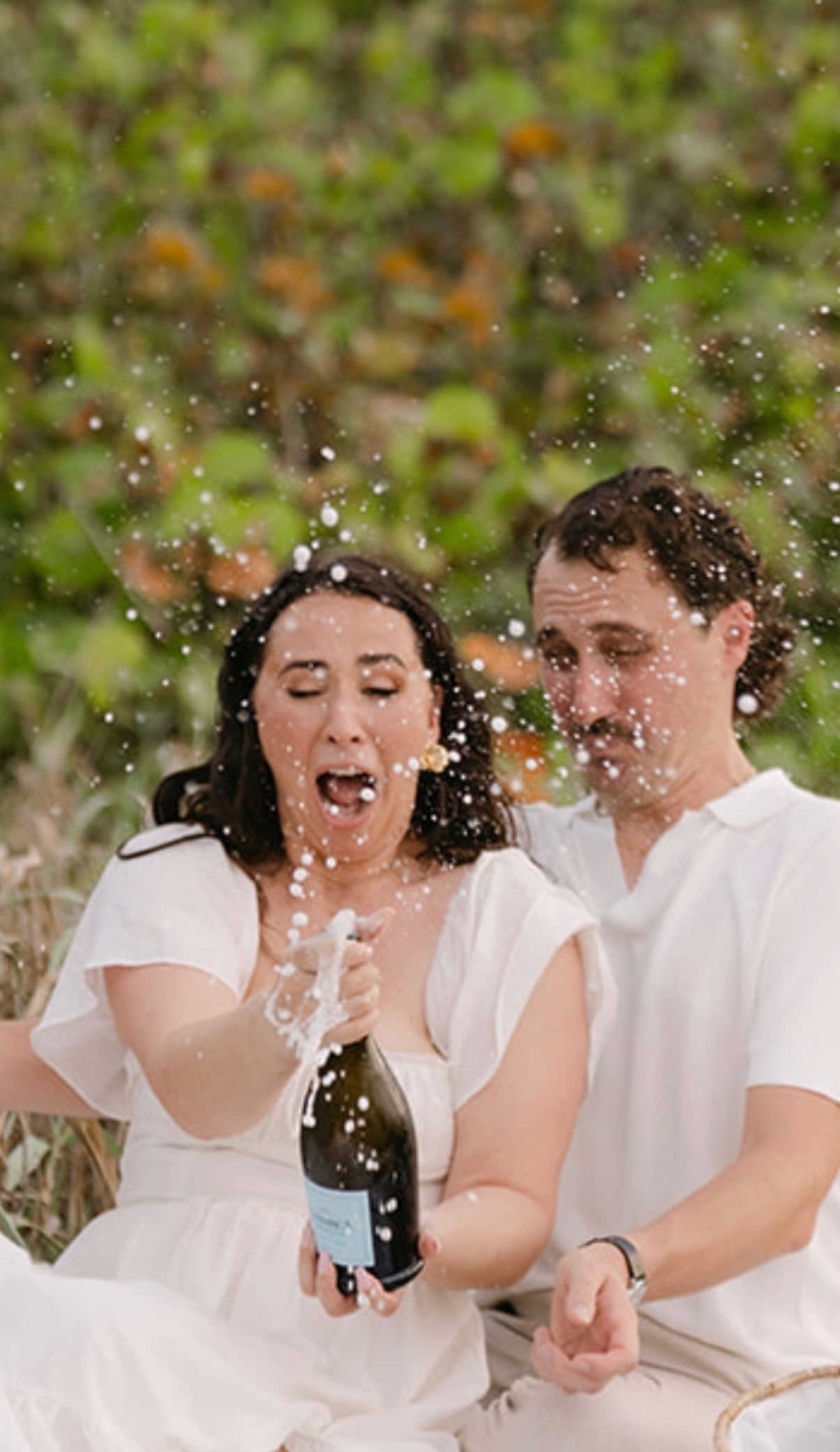 Claudia opening a bottle of champagne with Marcus beside her.