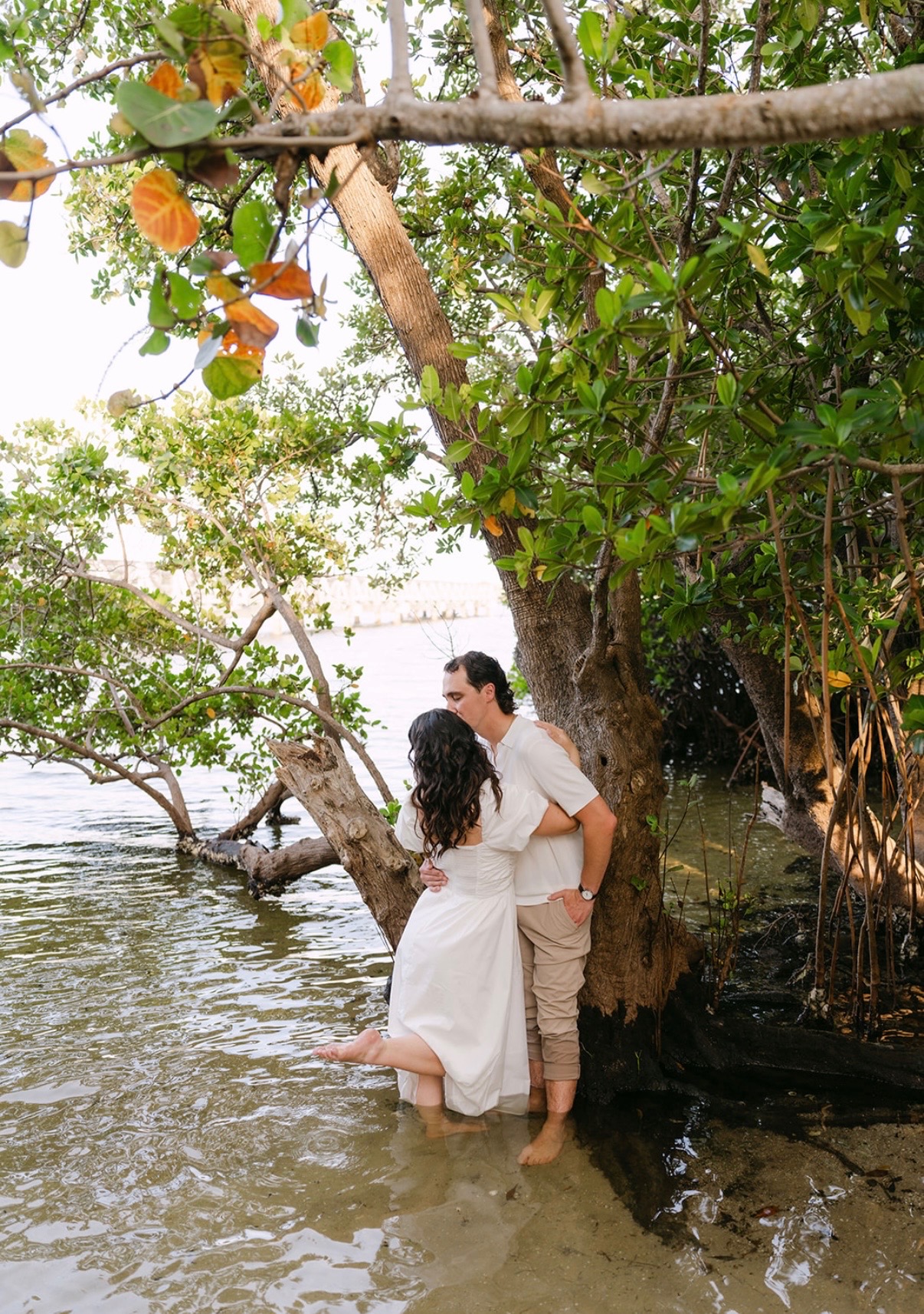 Claudia and Marcus kissing beside a mangrove tree.