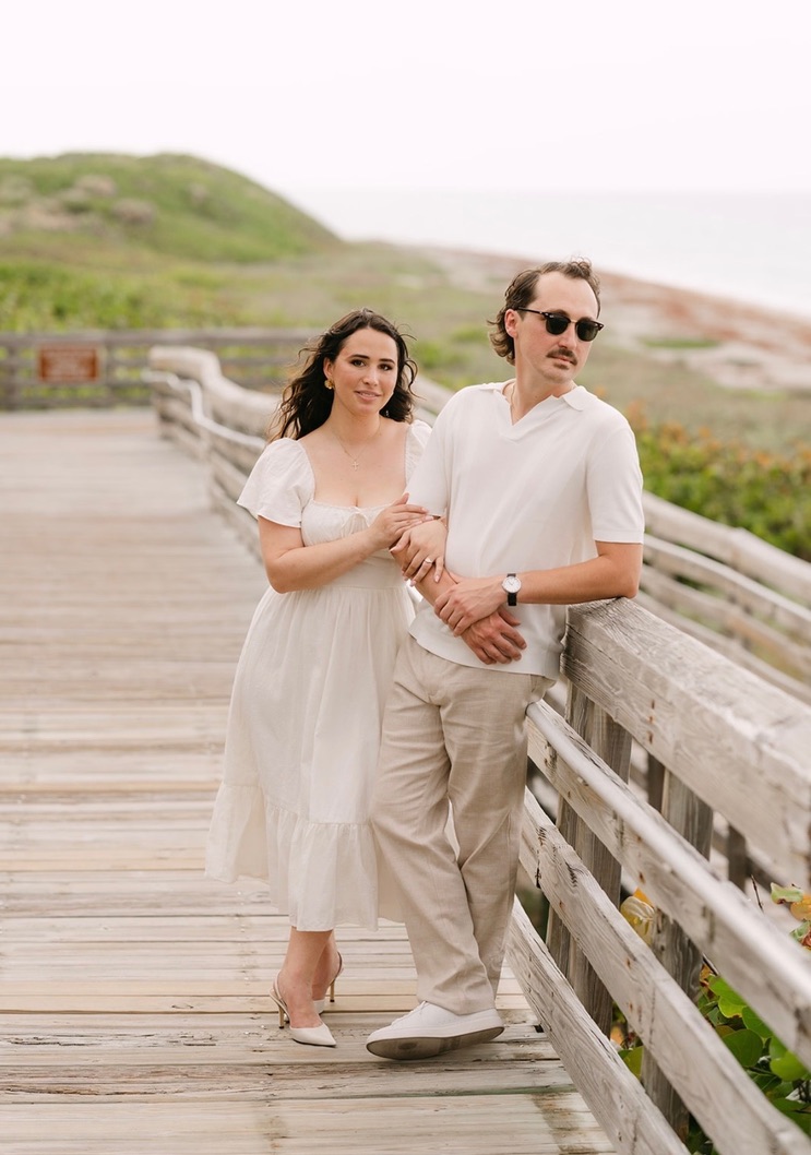 Claudia and Marcus standing close on a pale wooden boardwalk.
