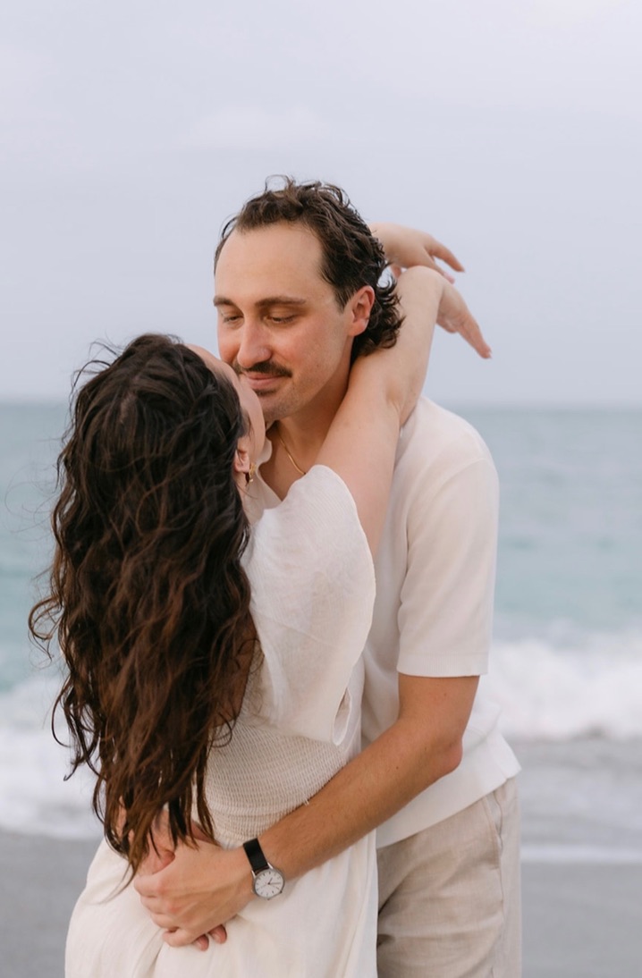 Claudia and Marcus leaning in for a kiss beside the ocean.