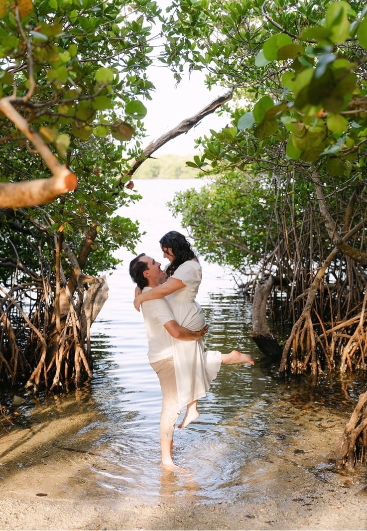 Claudia and Marcus laughing in the water between mangrove roots.