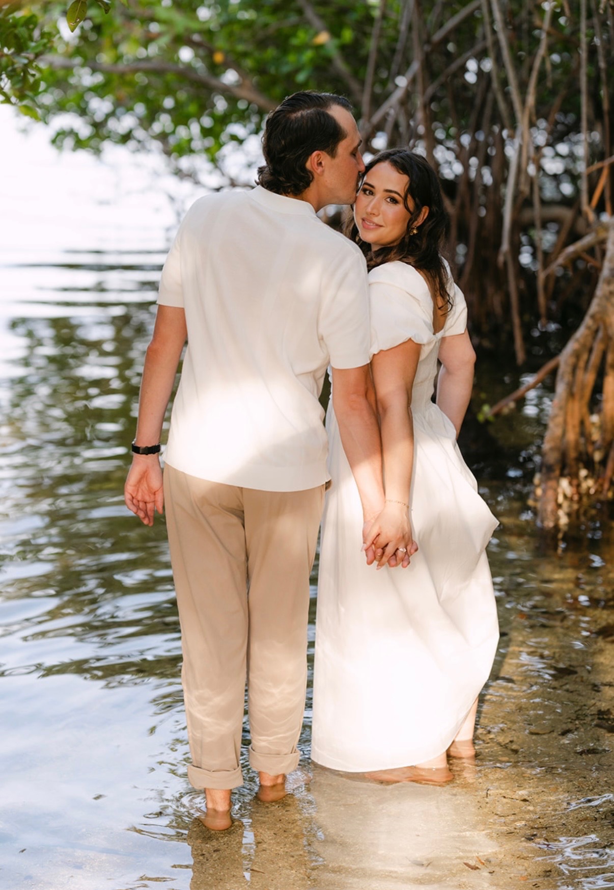 Marcus kissing Claudia's cheek as they hold hands in the water.