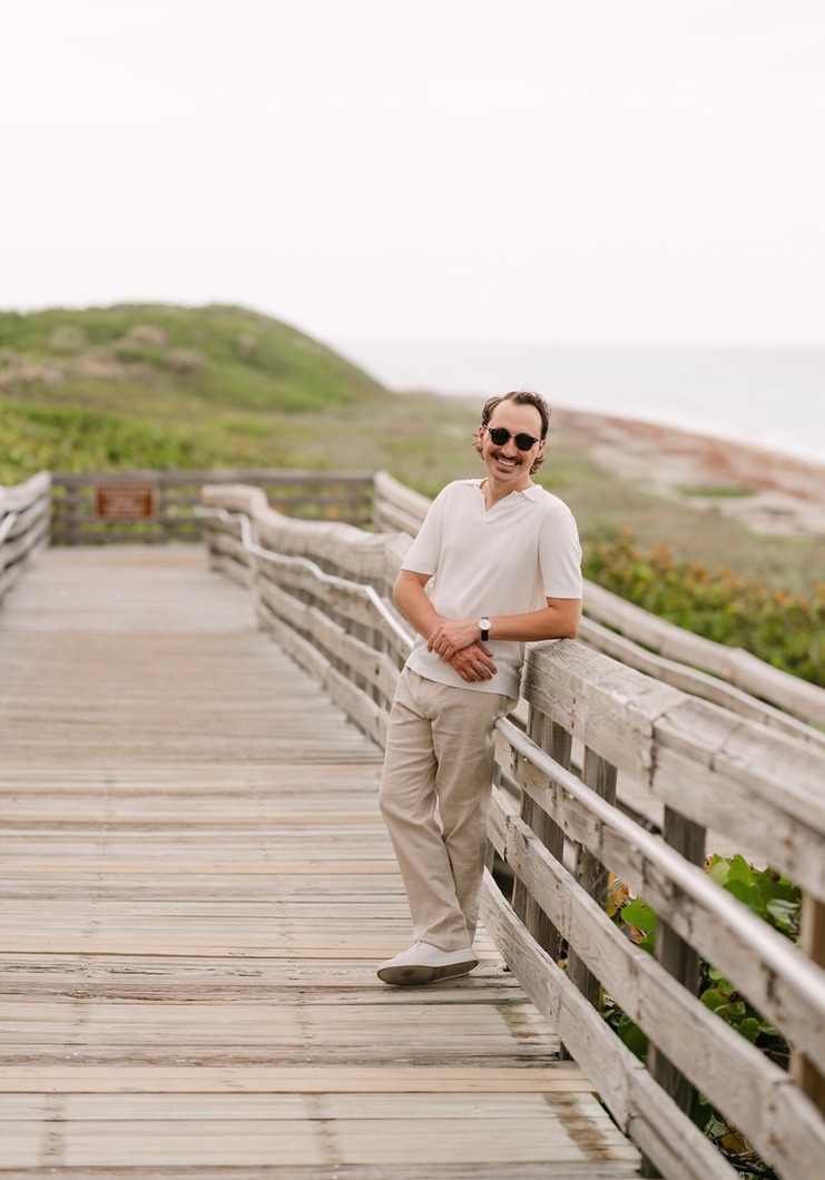 Marcus leaning against the boardwalk rail near the ocean.