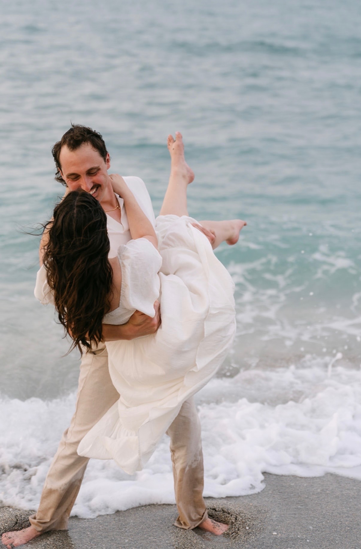 Marcus carrying Claudia beside the ocean waves.