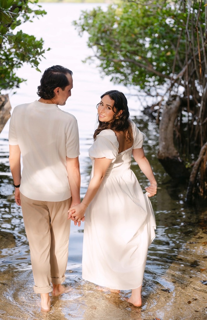 Claudia looking back while holding Marcus's hand in shallow water.